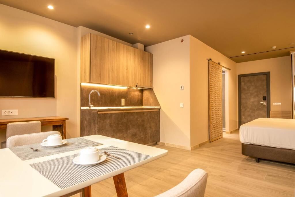 A compact hotel room with a kitchenette, a dining area with a table and chairs, and a bed.