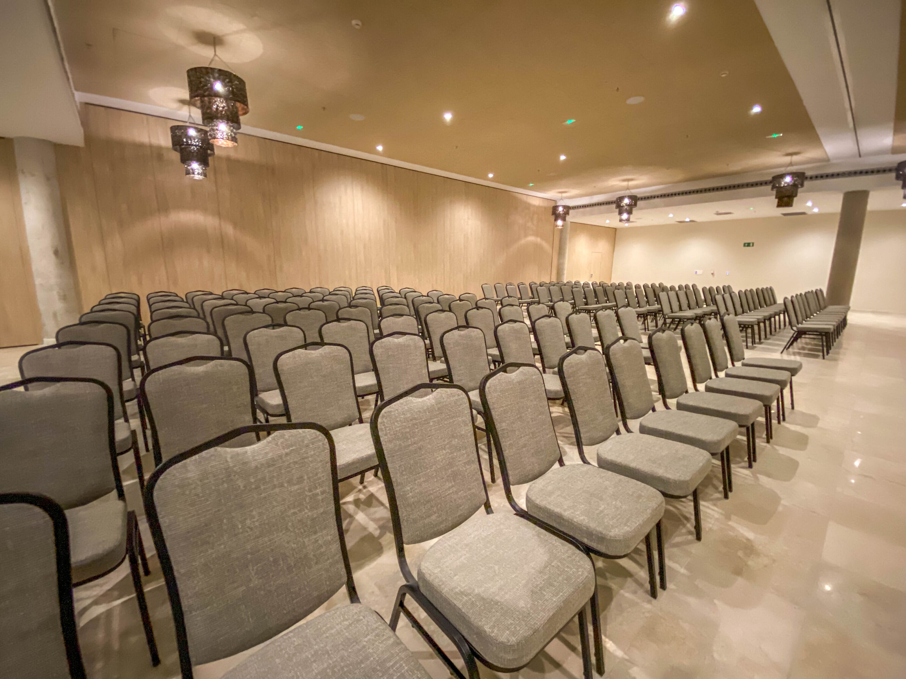 Une salle de conférence avec des rangées de chaises grises et un mur en bois.