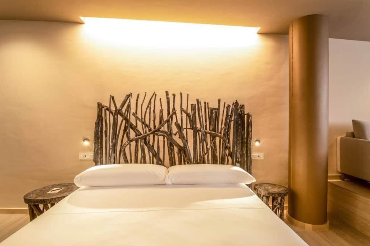 A hotel room with a bed, a wooden headboard, two bedside tables, and a wall-mounted light.