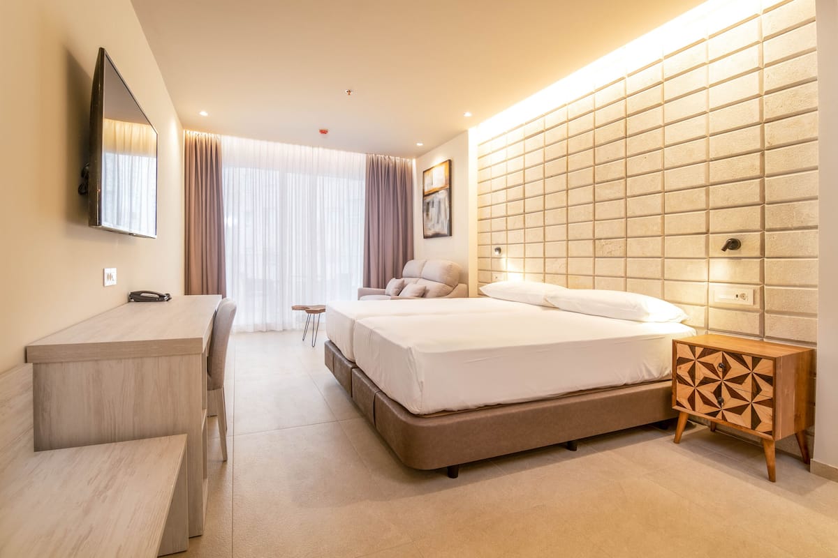 A modern hotel room with a large bed, a desk, and a bedside table.