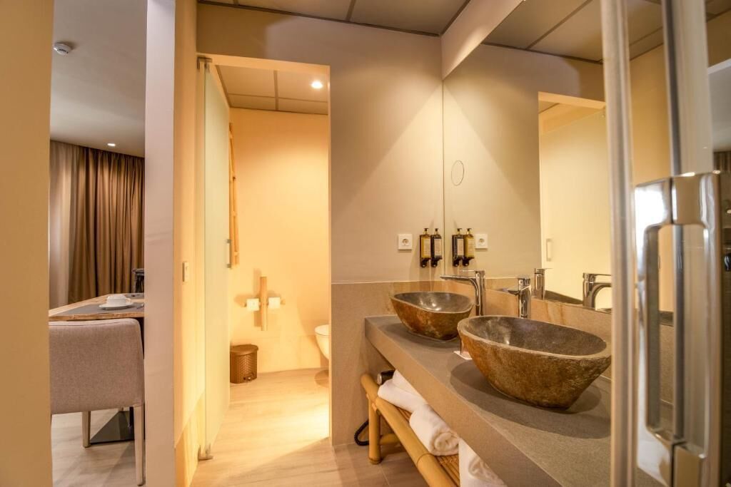 A modern bathroom with two large stone sinks, a mirror, and a wooden bench.