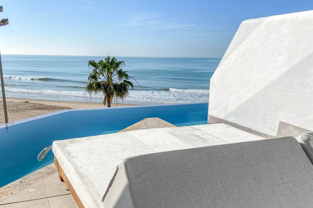 A bed with a view of the ocean and a palm tree.