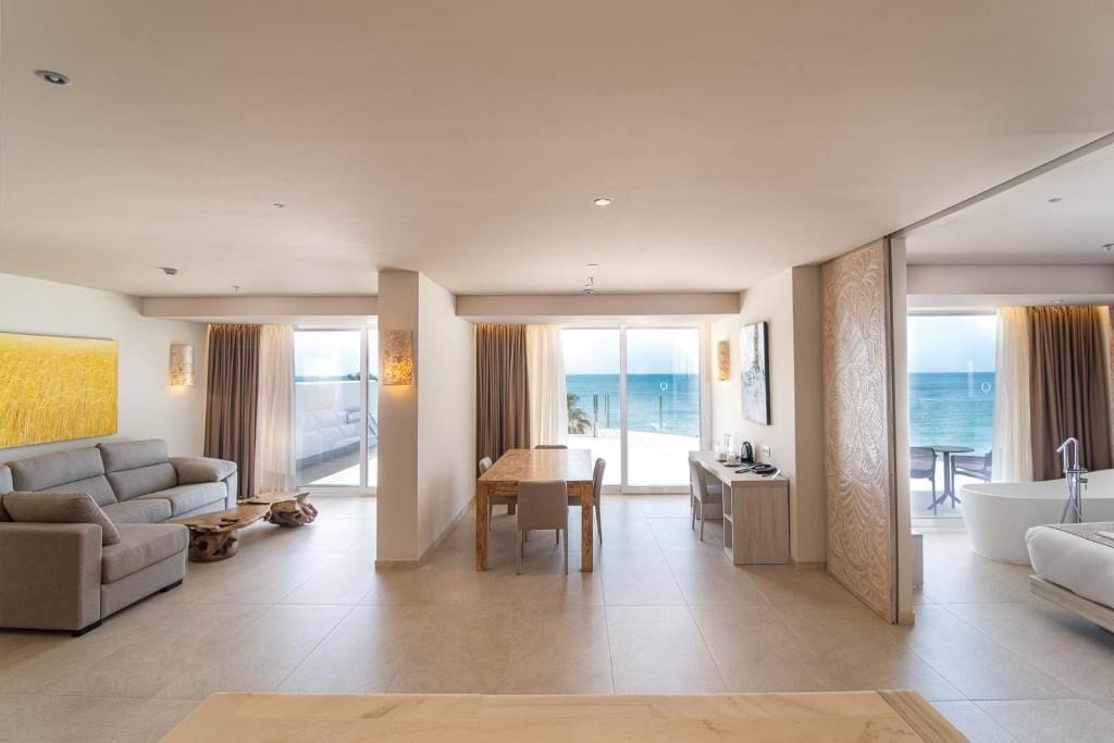 A spacious living room with a large window overlooking the sea, a dining area, and a modern kitchen.