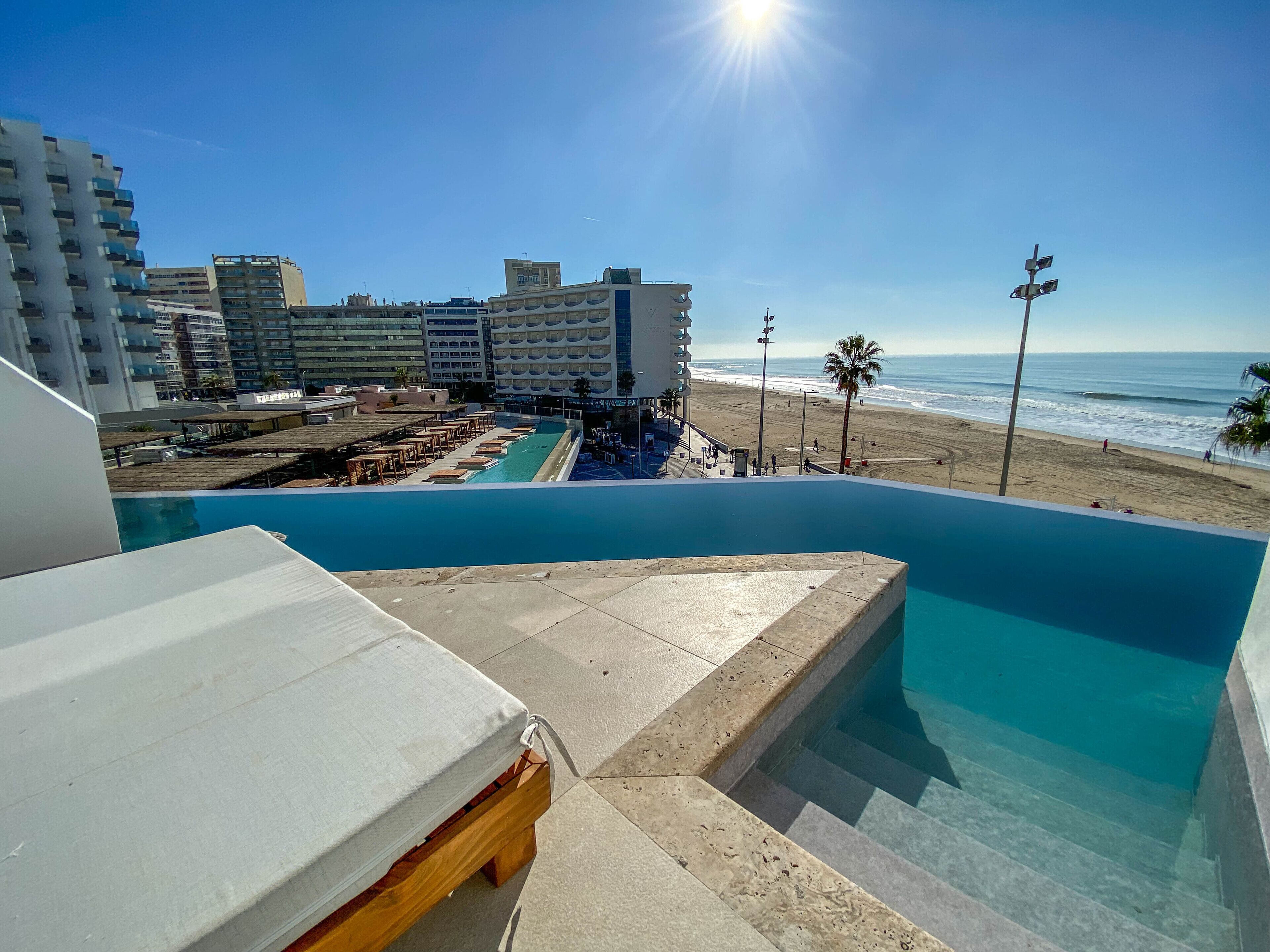 Una piscina con vista sulla spiaggia e sull'oceano, circondata da edifici di un hotel.