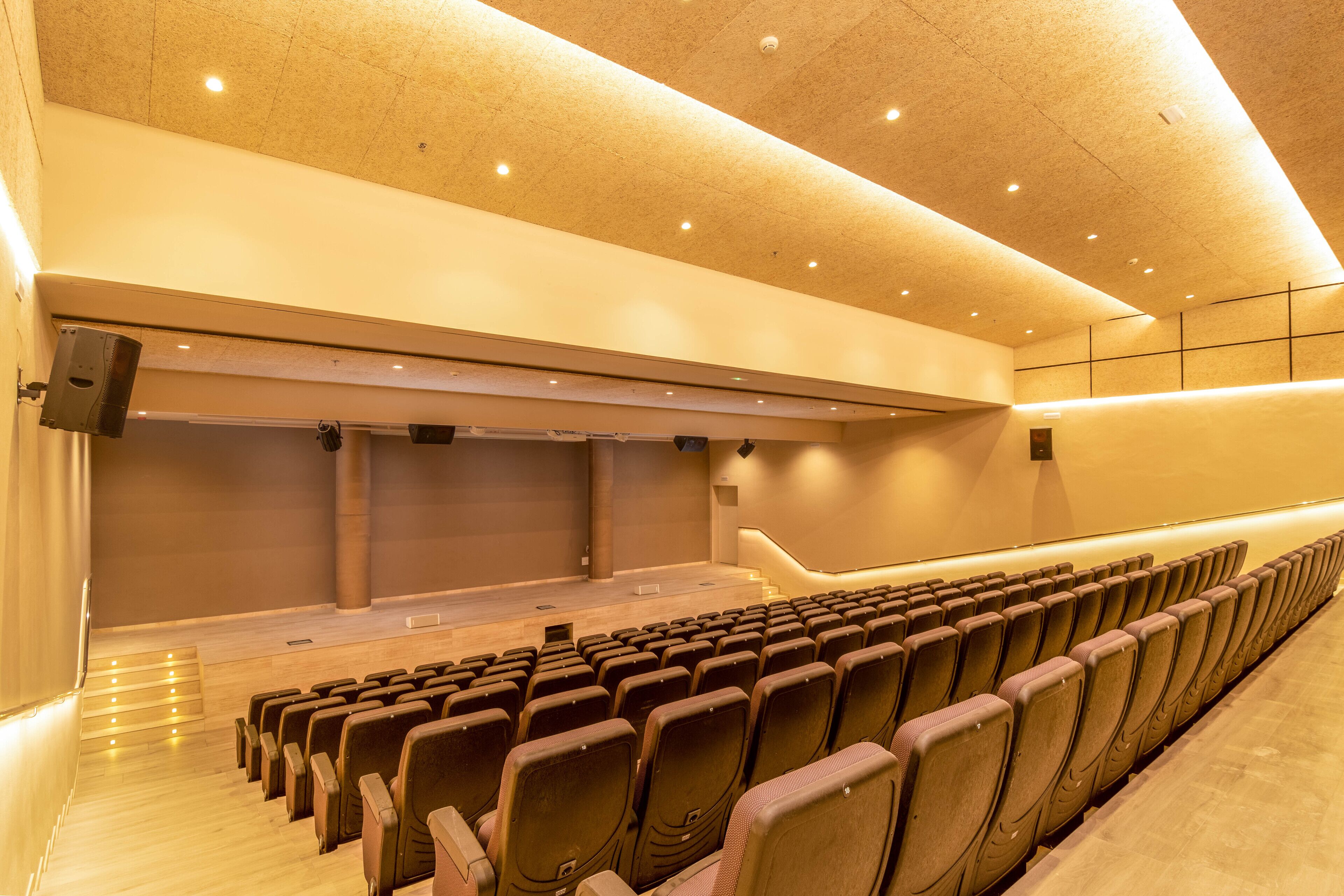 Un auditorio interior con hileras de asientos, un escenario e iluminación empotrada en el techo.