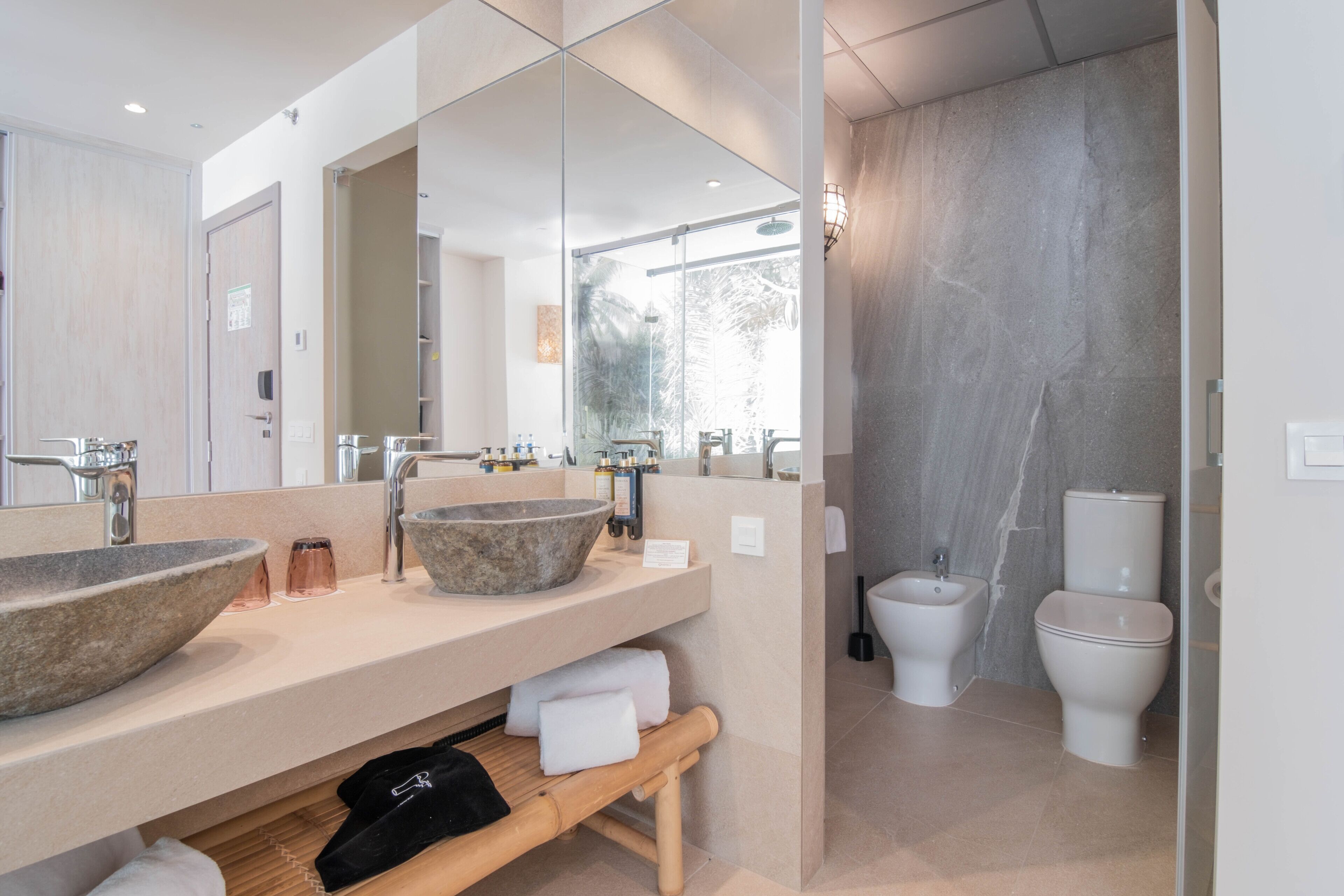 Ein modernes Badezimmer mit einem großen Spiegel, zwei Waschbecken mit Steinbecken, einem Bidet und einer Toilette.