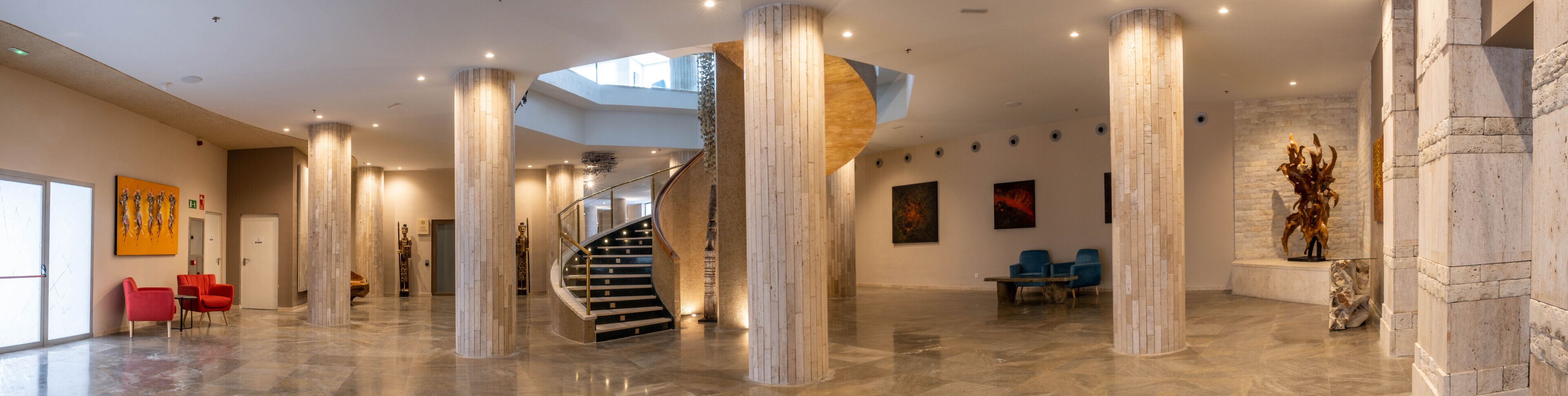 Eine geräumige Lobby mit hohen Decken, einer zentralen Treppe und modernen Möbeln.