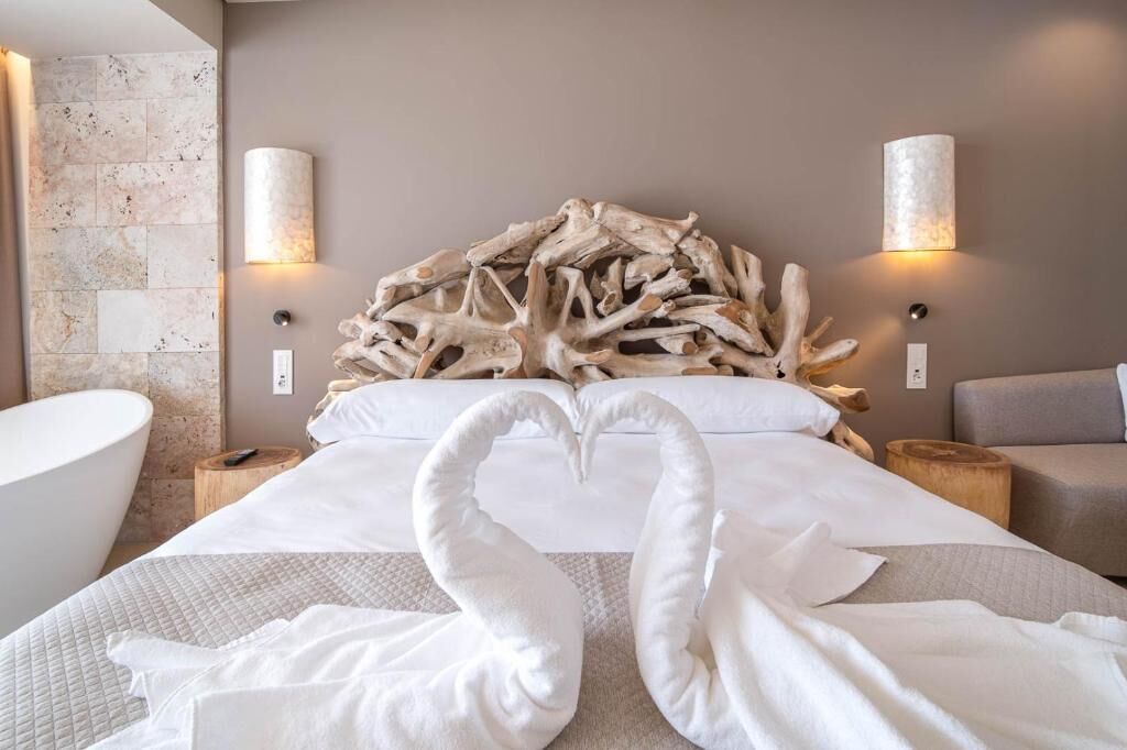 A hotel room with a large bed, two wall-mounted lamps, a wooden headboard, and a bathtub.