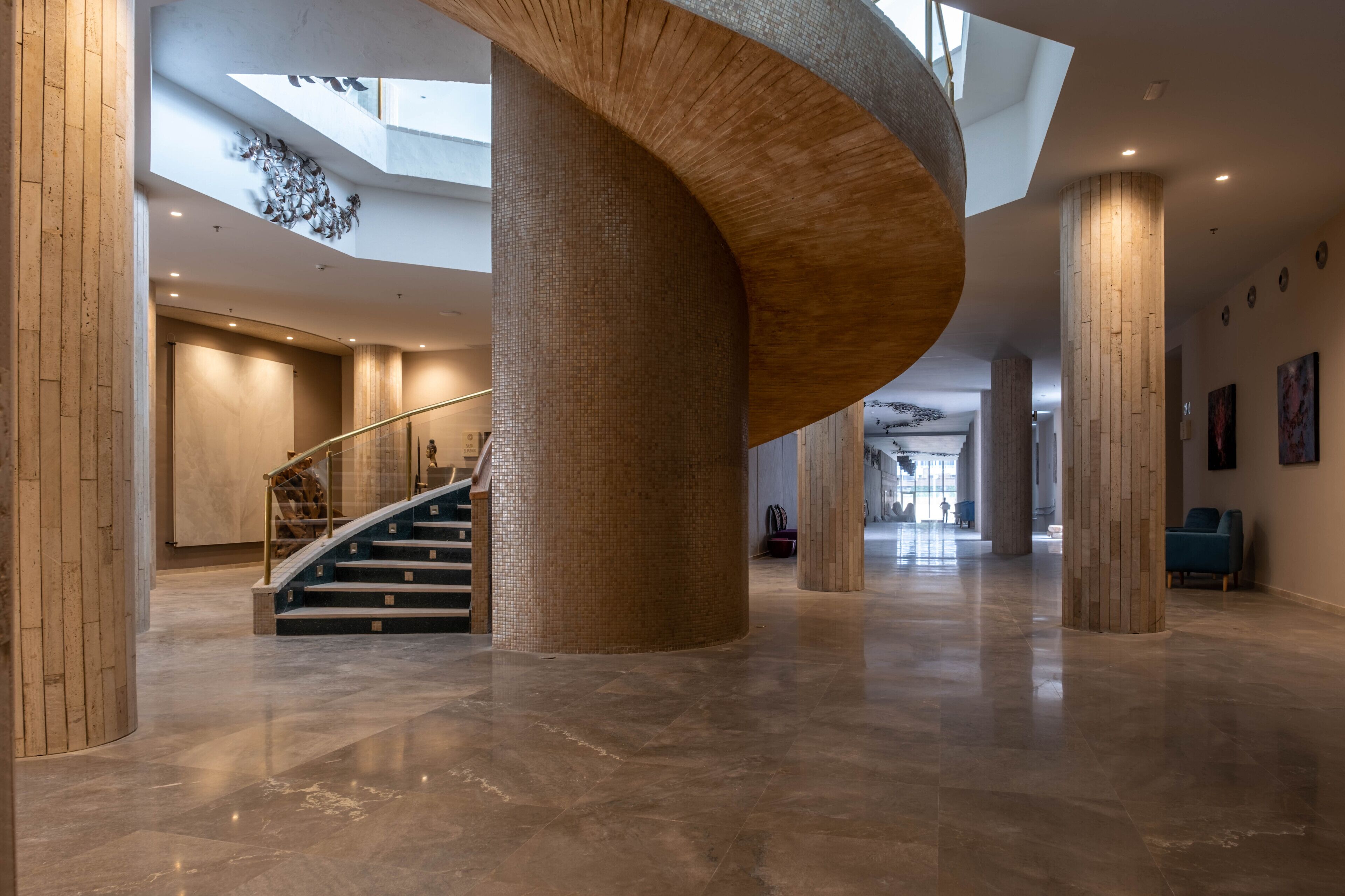 A spacious lobby with a curved wooden column, a staircase, and a high ceiling with skylights.