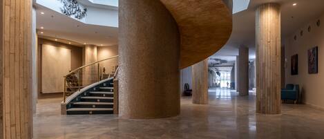 A spacious lobby with a curved wooden column, a staircase, and a high ceiling with skylights.