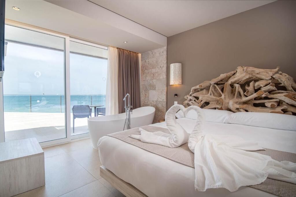 A modern hotel room with a large bed, a bathtub, and a view of the sea.
