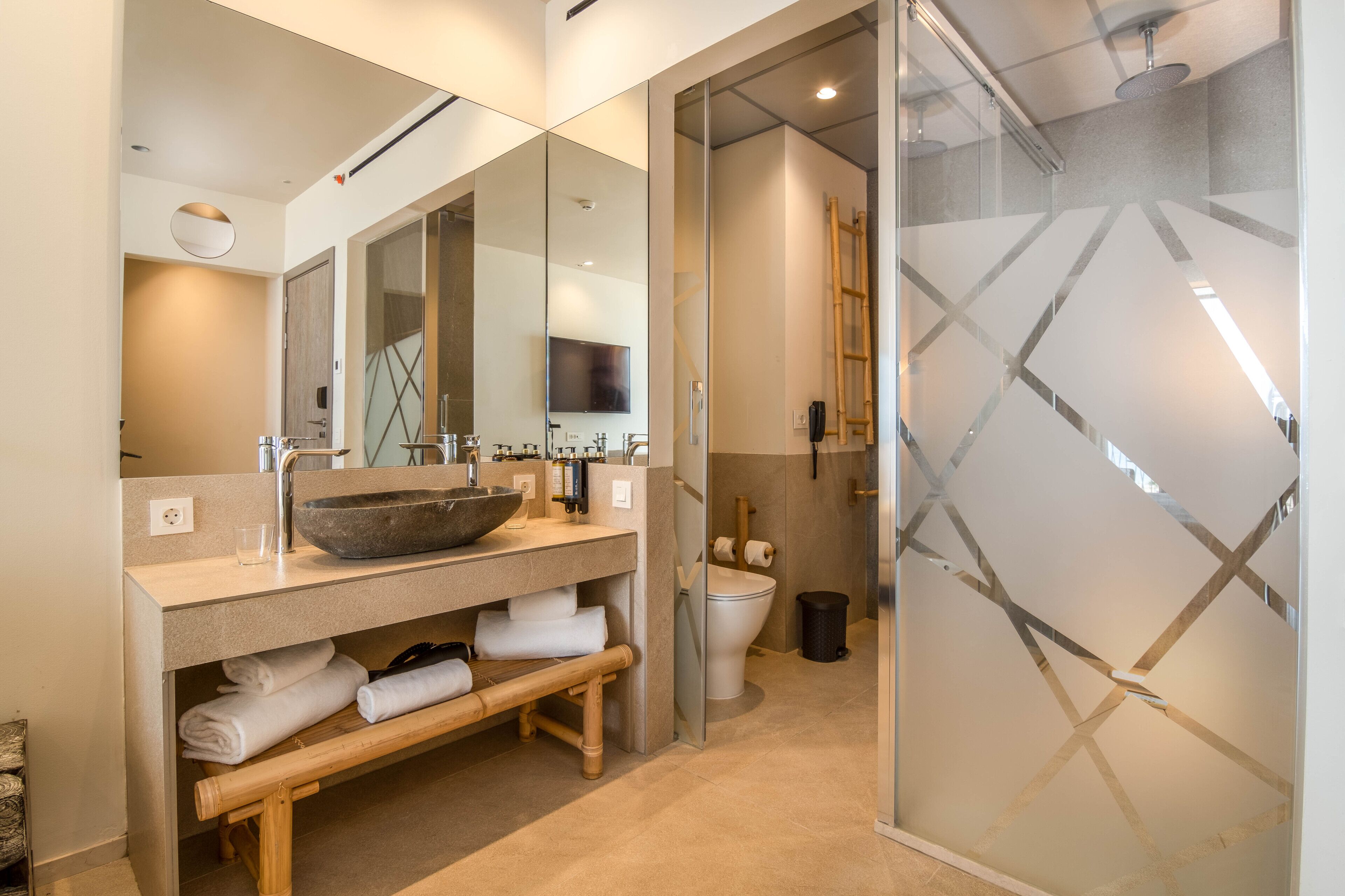 A modern bathroom with a large mirror, a bowl sink, a toilet, and a shower area.