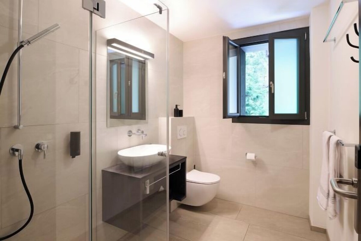 Un baño moderno con ducha de vidrio, un lavamanos blanco y un inodoro.