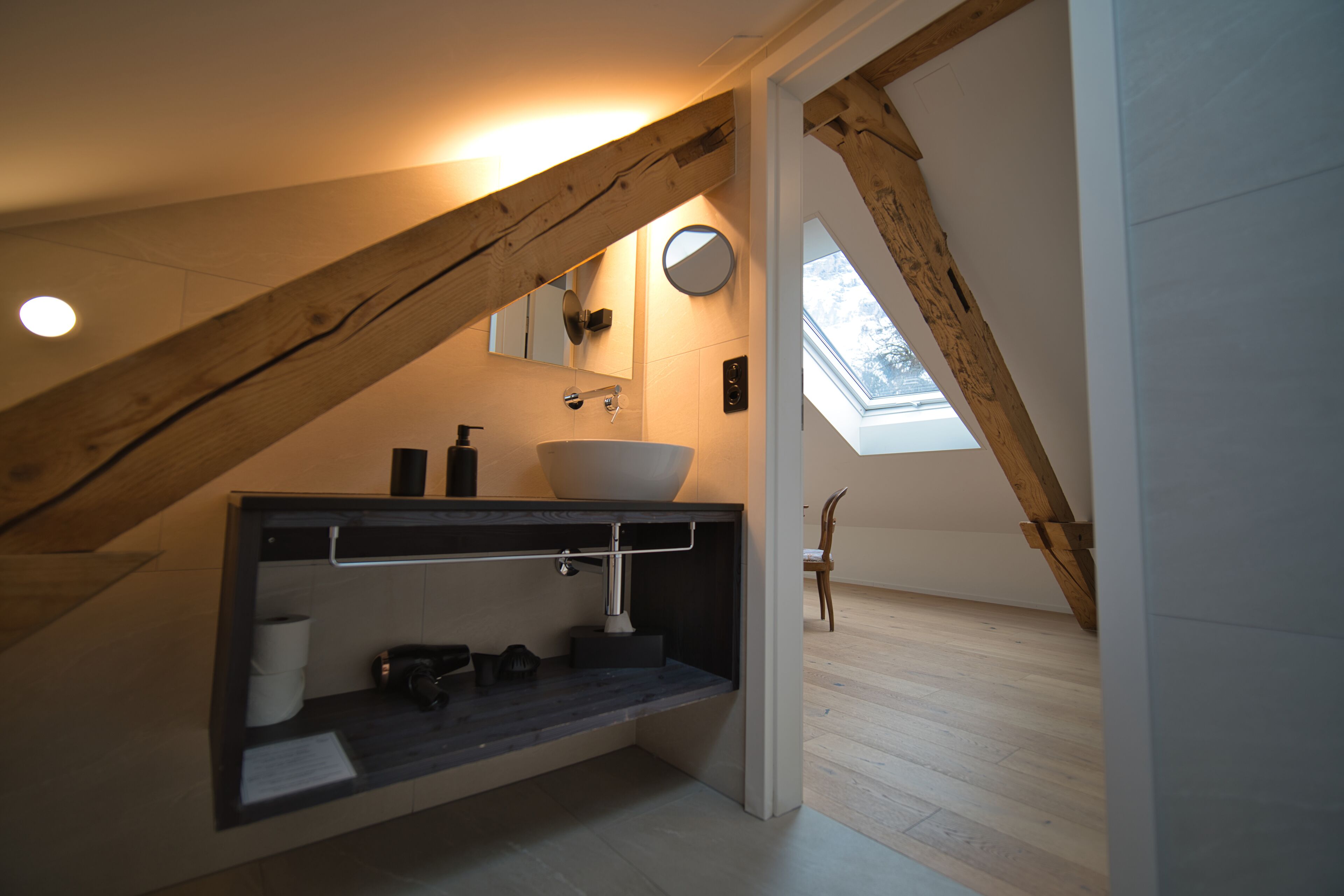 Een moderne badkamer met dakraam, houten balken en een ingebouwd wastafel.
