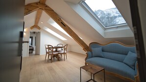 A room with a sloped ceiling, wooden beams, a dining table with chairs, a sofa, and a skylight. - EVAL Grindelwald AG (Grindelwald)