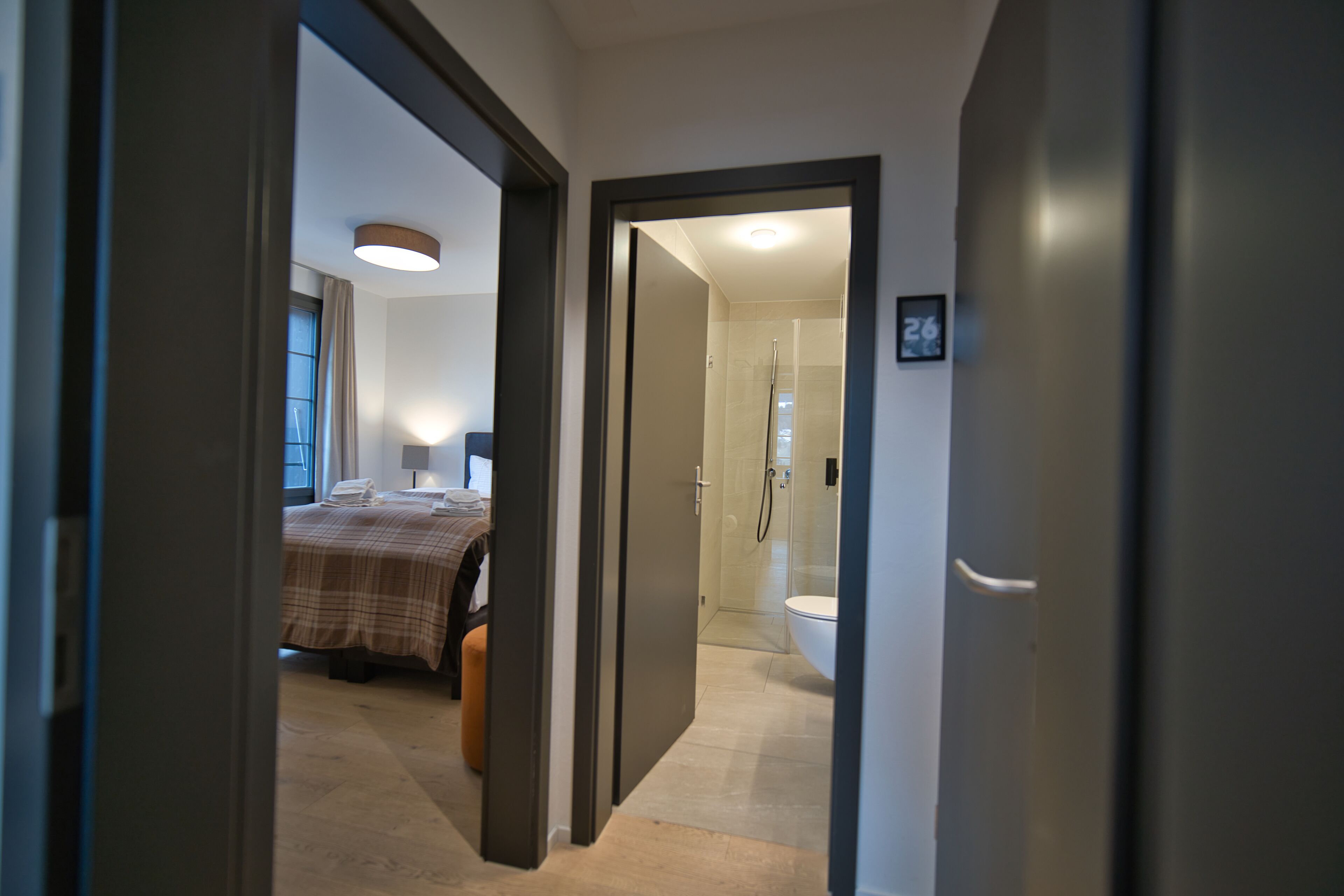A hotel room with a bed, a bedside table, a lamp, and a bathroom with a shower and toilet.