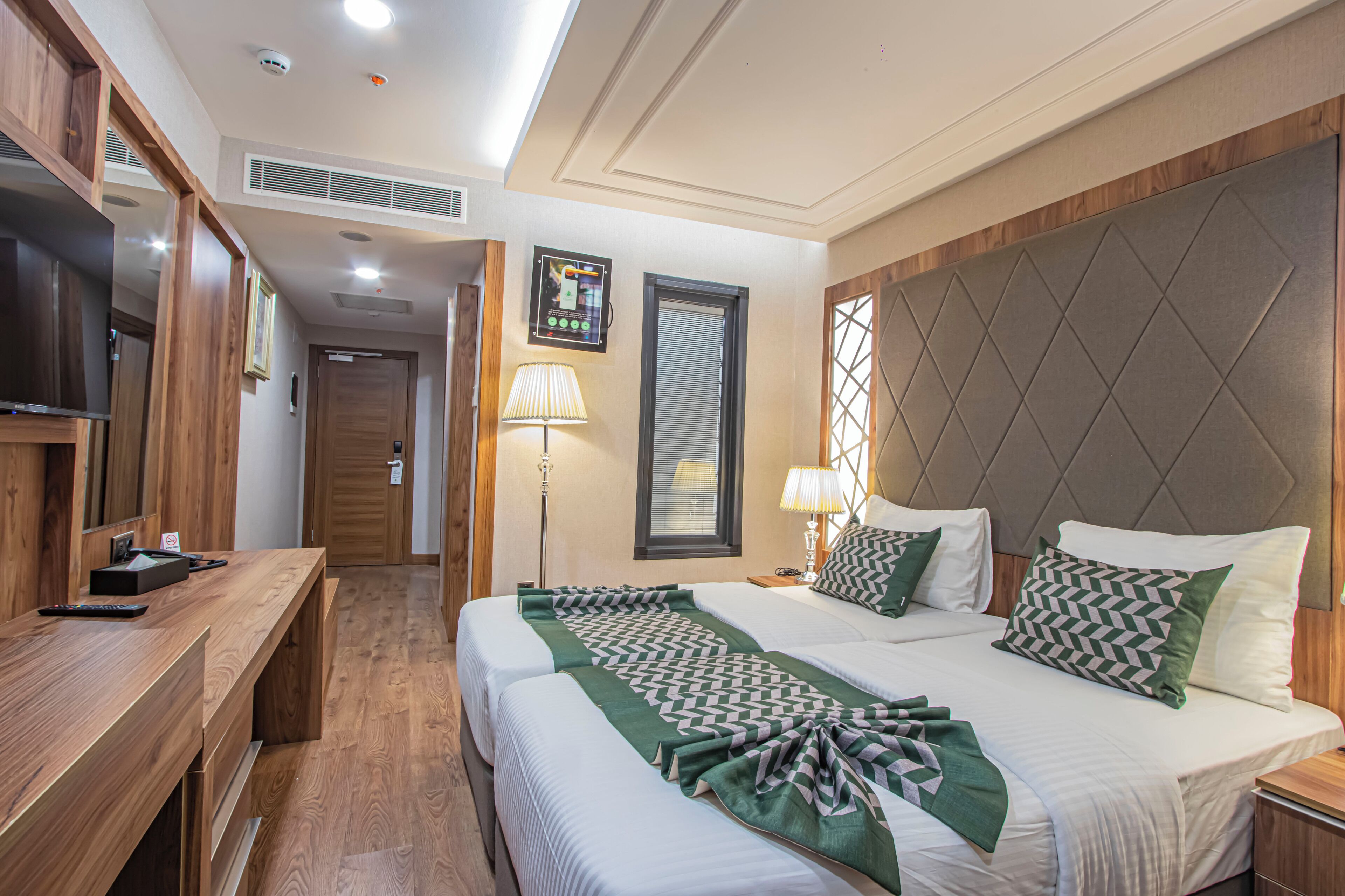 A hotel room with a large bed, a wooden desk, a television, and a wall-mounted TV.