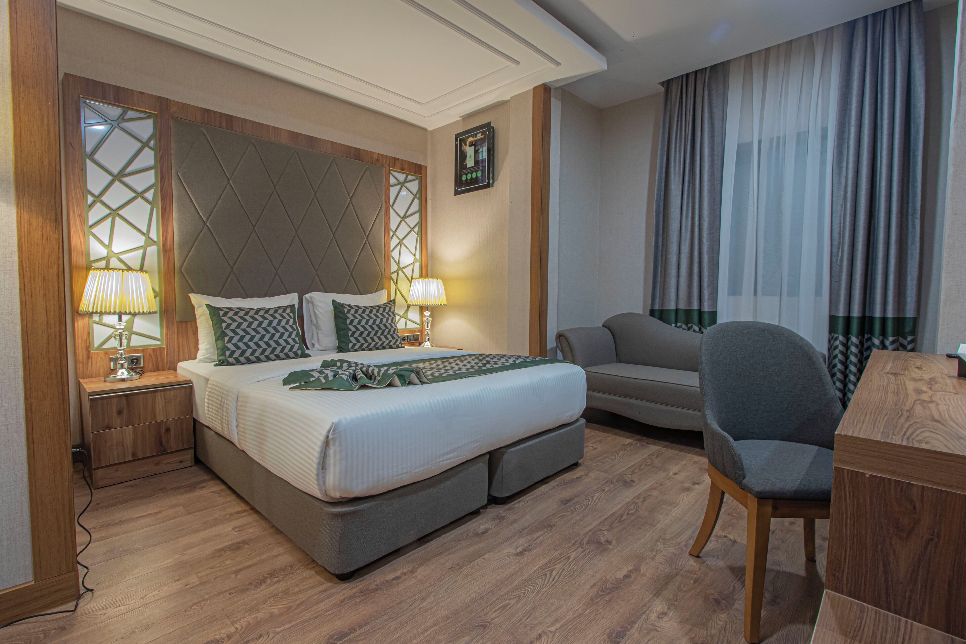 Une chambre d’hôtel avec un lit, des tables de chevet, un bureau, une chaise et une grande fenêtre avec des rideaux.