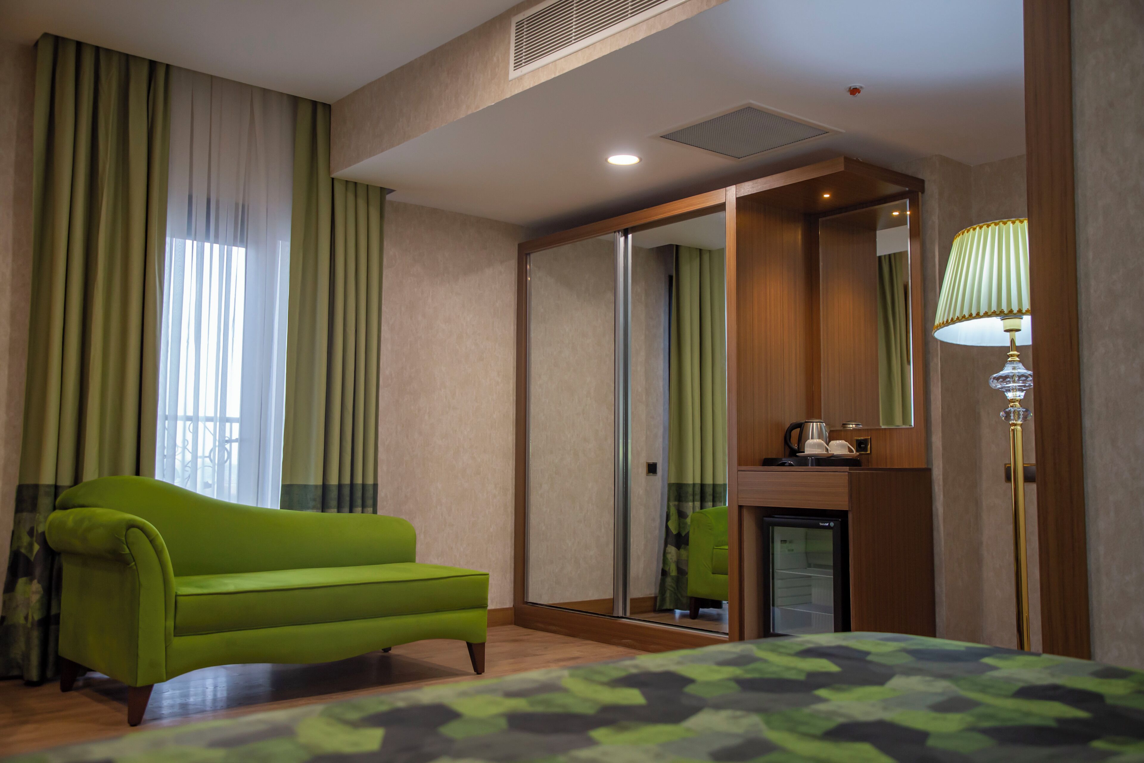 Une chambre d’hôtel avec un canapé vert, un lit recouvert d’une courtepointe à motifs de camouflage, un miroir, une lampe et un mini-réfrigérateur.