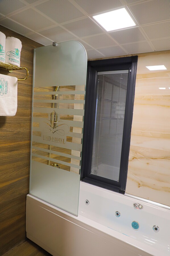 Un baño con mampara de vidrio, bañera y ventana con persianas.