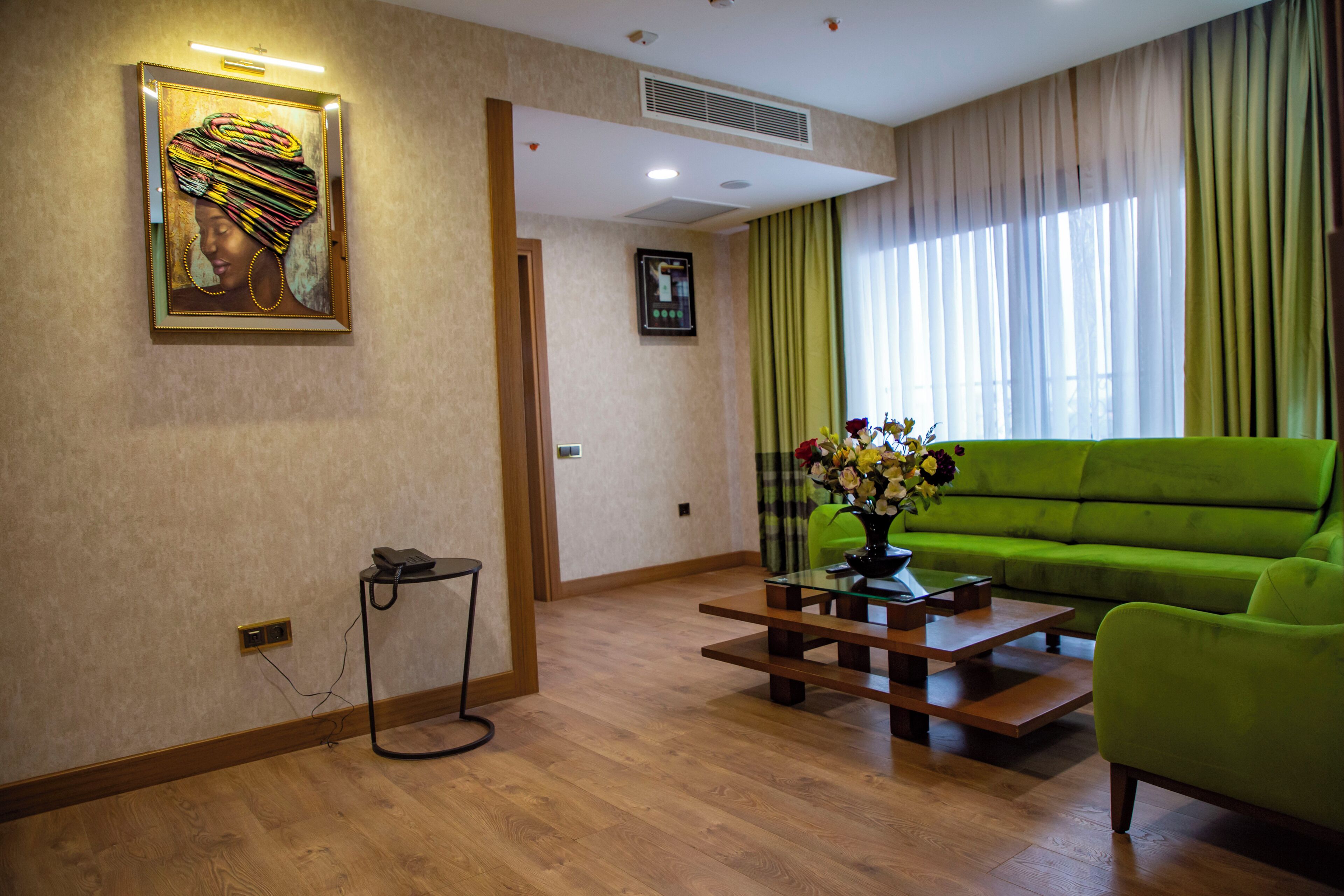 Una sala de estar con un sofá verde, una mesa de centro de madera con un jarrón de flores, una obra de arte enmarcada en la pared y un teléfono sobre un pedestal.
