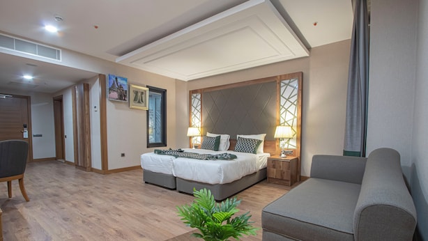 Et moderne hotelværelse med dobbeltseng, sofa, spisebord og en potteplante.