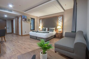 A modern hotel room with a double bed, a sofa, a dining table, and a potted plant. - United Hotel International (Yaoundé)