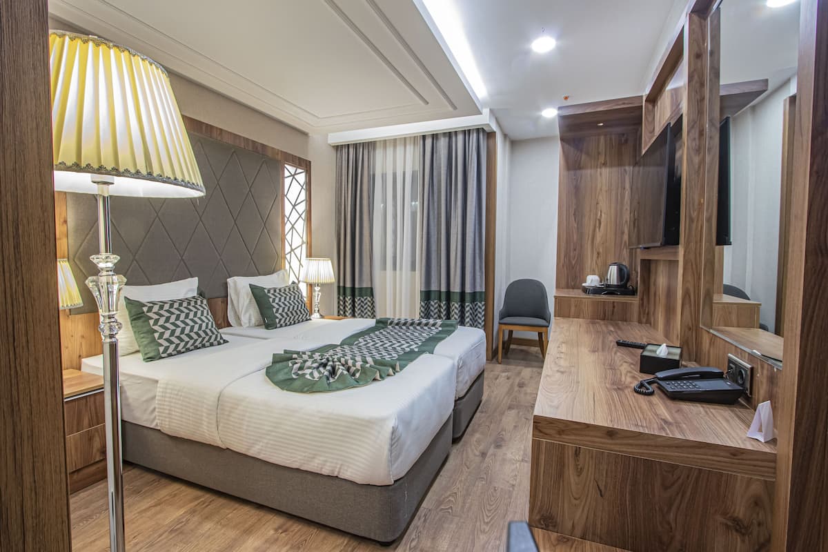 A hotel room with a bed, bedside lamps, a desk with a telephone, and a mirror.
