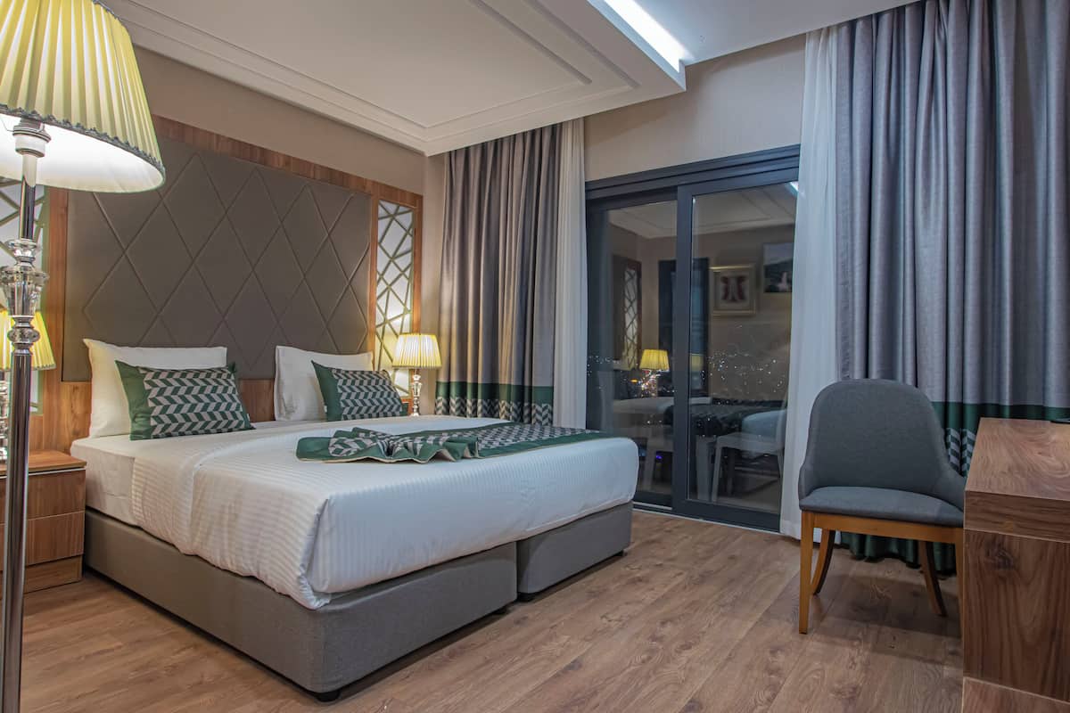 A hotel room with a large bed, a chair, a desk, and a view through a glass door.