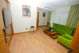 Una sala de estar con un sofá verde, una mesa de centro de madera y un televisor de pantalla plana montado en la pared.