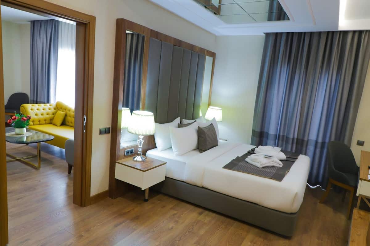A modern hotel room with a bed, bedside lamps, a small table with a plant, a sofa, and a chair.