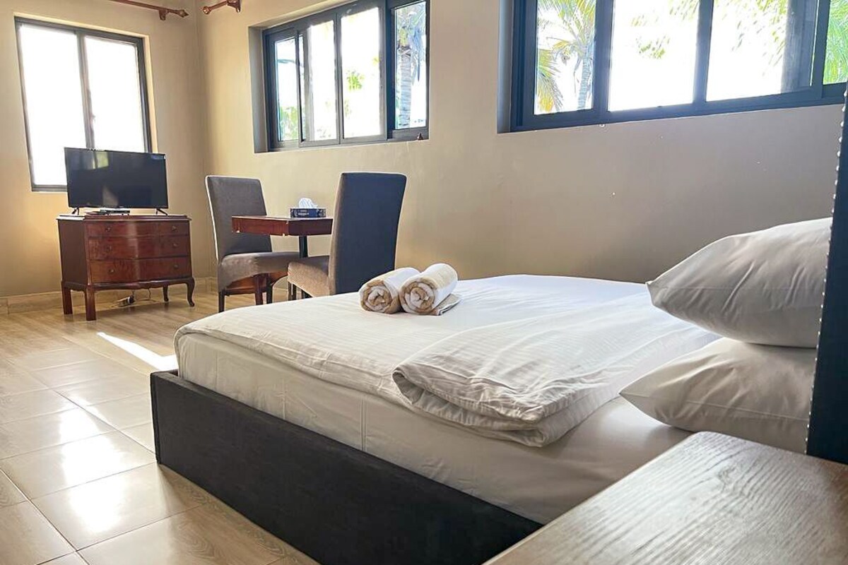Quarto com cama, escrivaninha, cadeira e televisão.