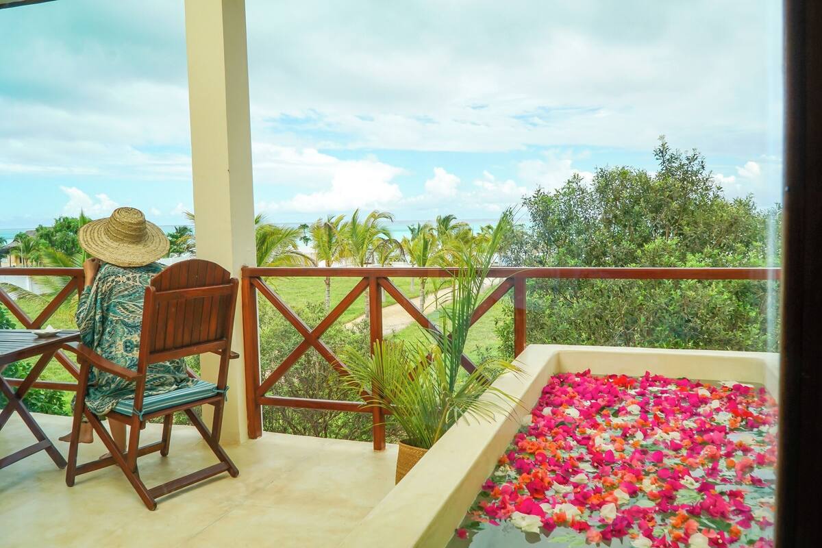 A balcony with a view of greenery and a flower-filled water feature.