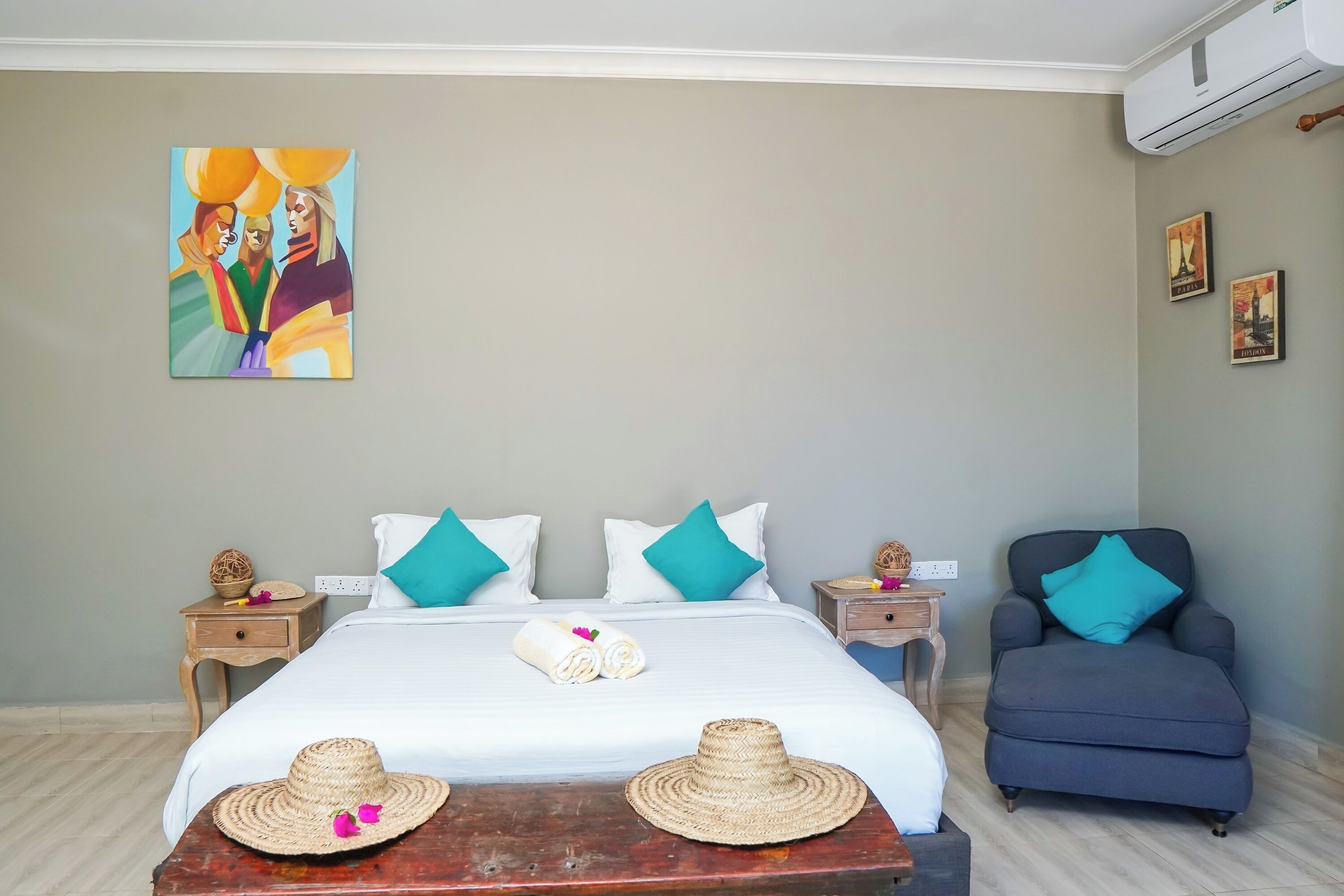 A bedroom with a bed, two nightstands, a chair, a painting, and a wall-mounted air conditioner.