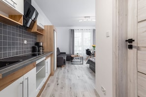 Eine moderne Küche mit schwarzer Arbeitsplatte, Holzschränken und einem eingebauten Backofen. Ein Essbereich mit Tisch und Stühlen sowie ein Sofa sind ebenfalls vorhanden.