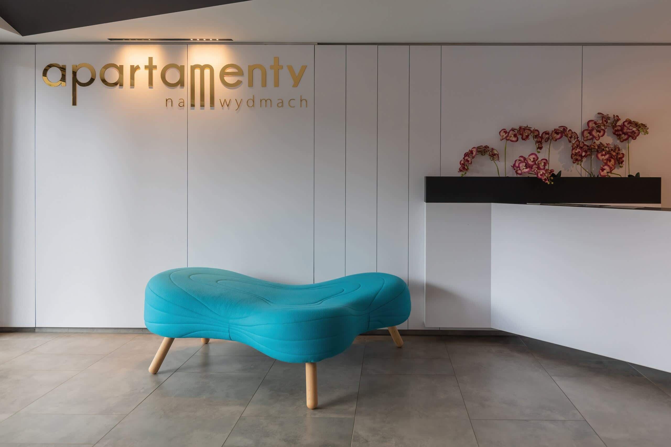 A modern reception area with a teal bench, a wall-mounted TV, and a sign reading "apartamentv nawydymach".