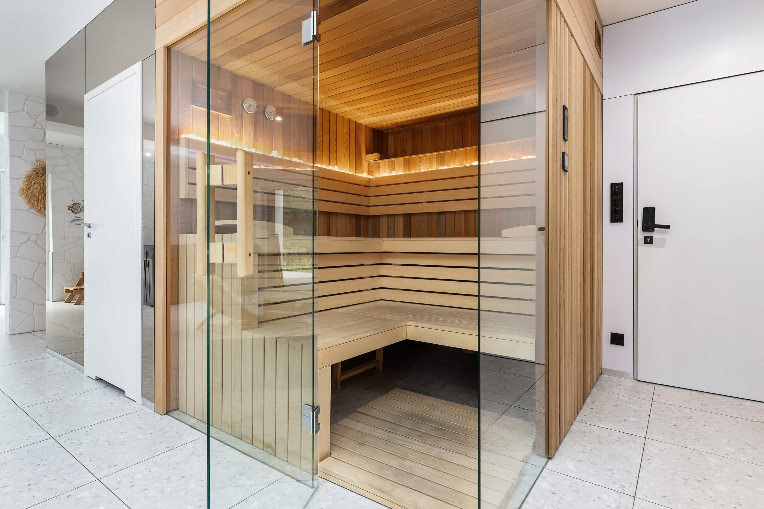 A modern sauna with glass walls, wooden benches, and a tiled floor.