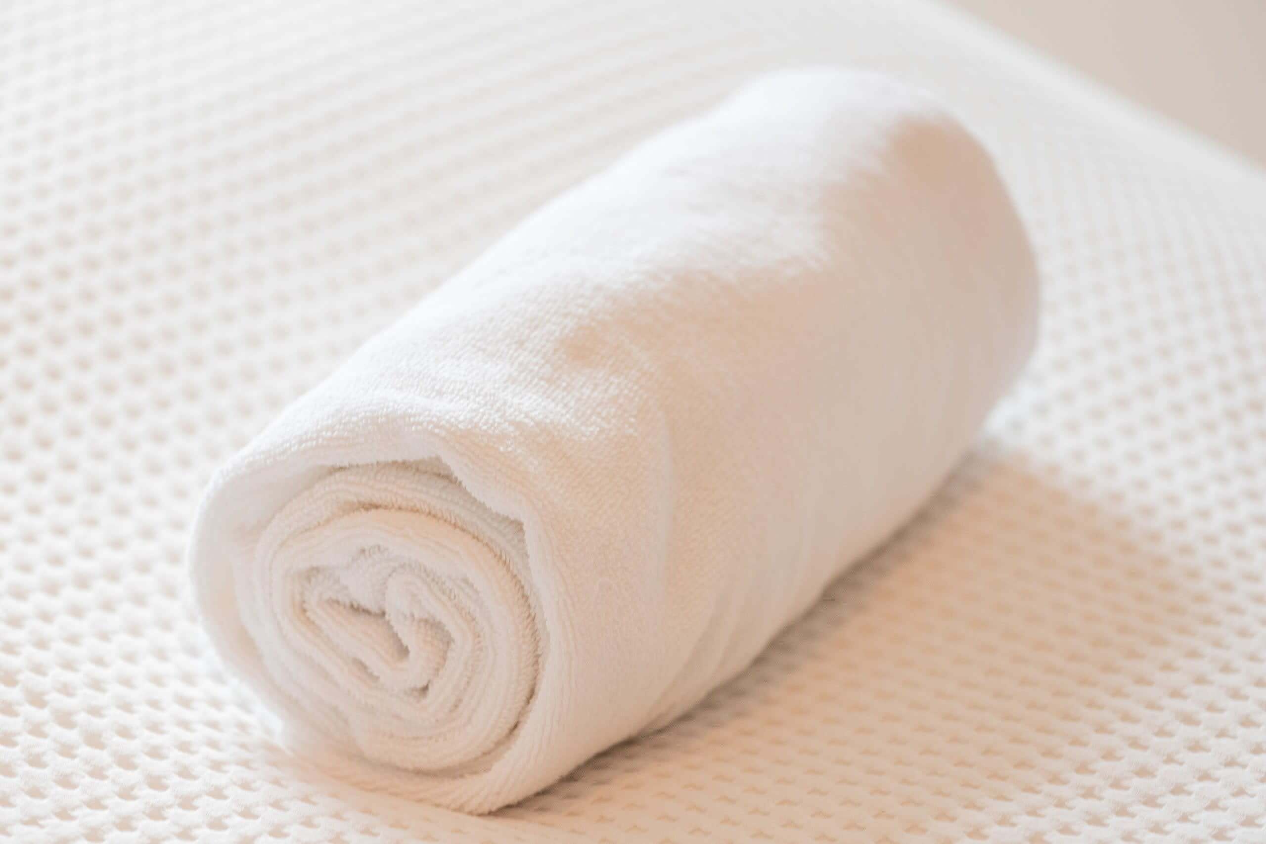 A rolled white towel on a textured white surface.