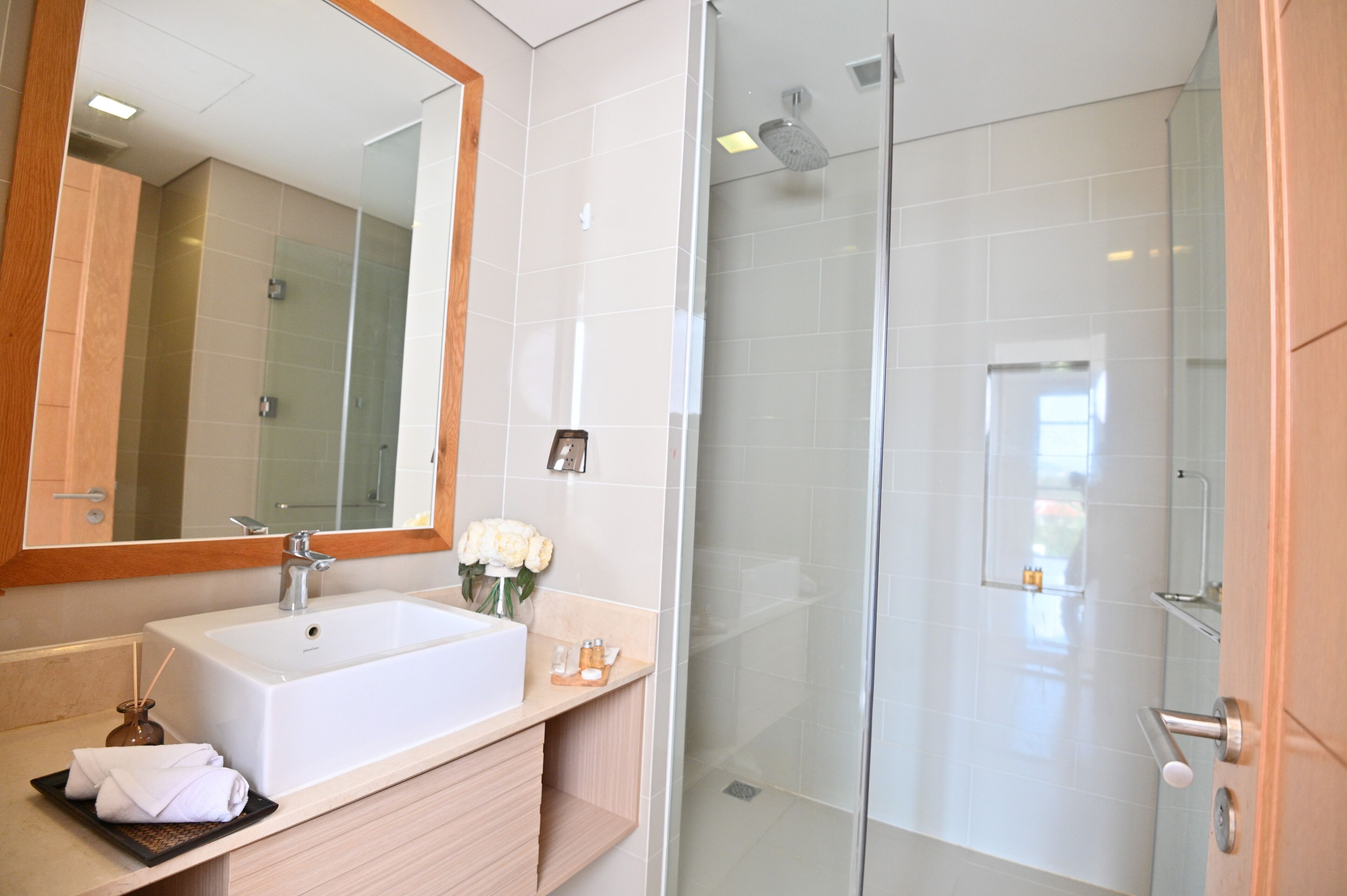 A modern bathroom with a large mirror, a white sink, and a glass-enclosed shower.