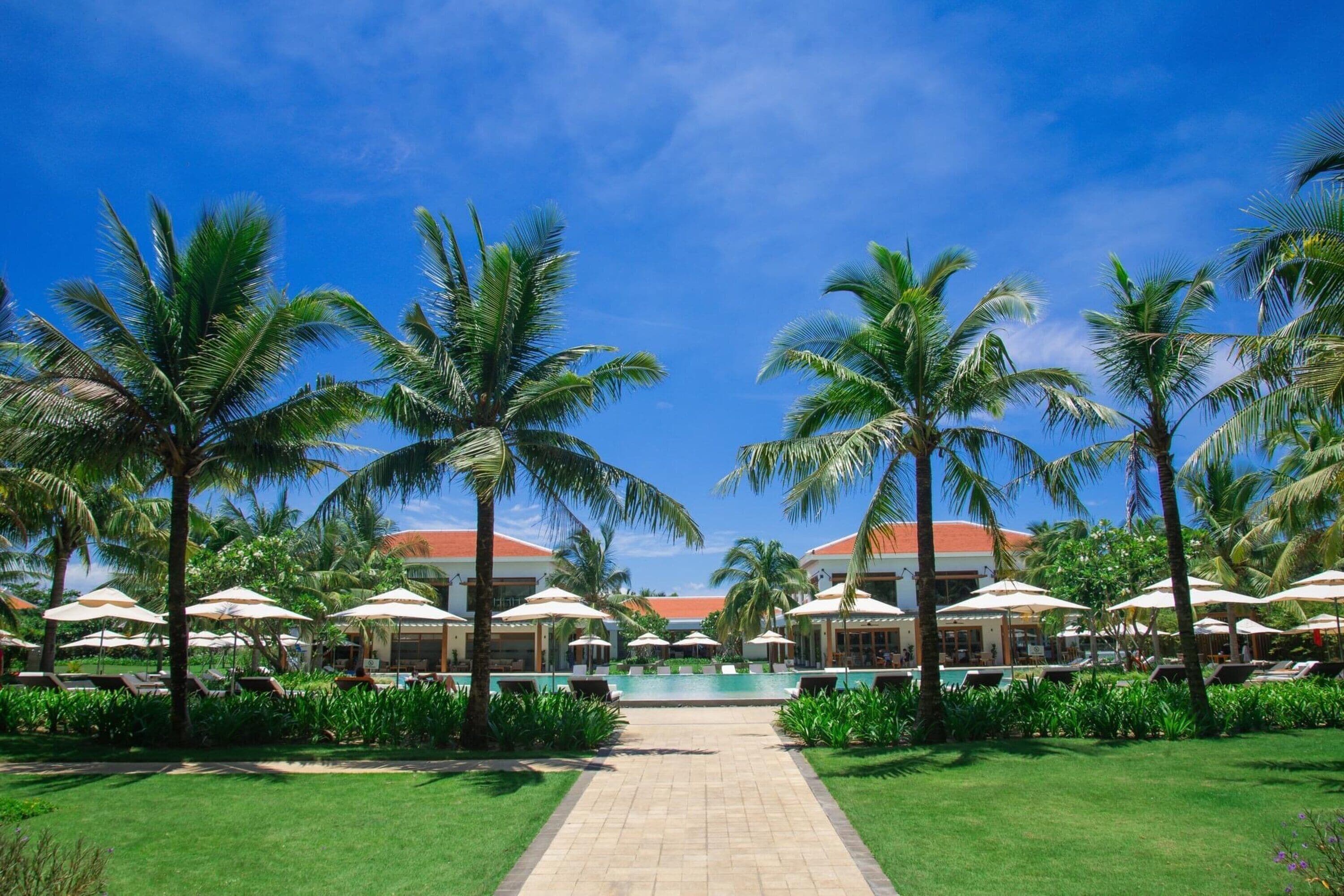 A resort pool area with palm trees, lounge chairs, and umbrellas.
