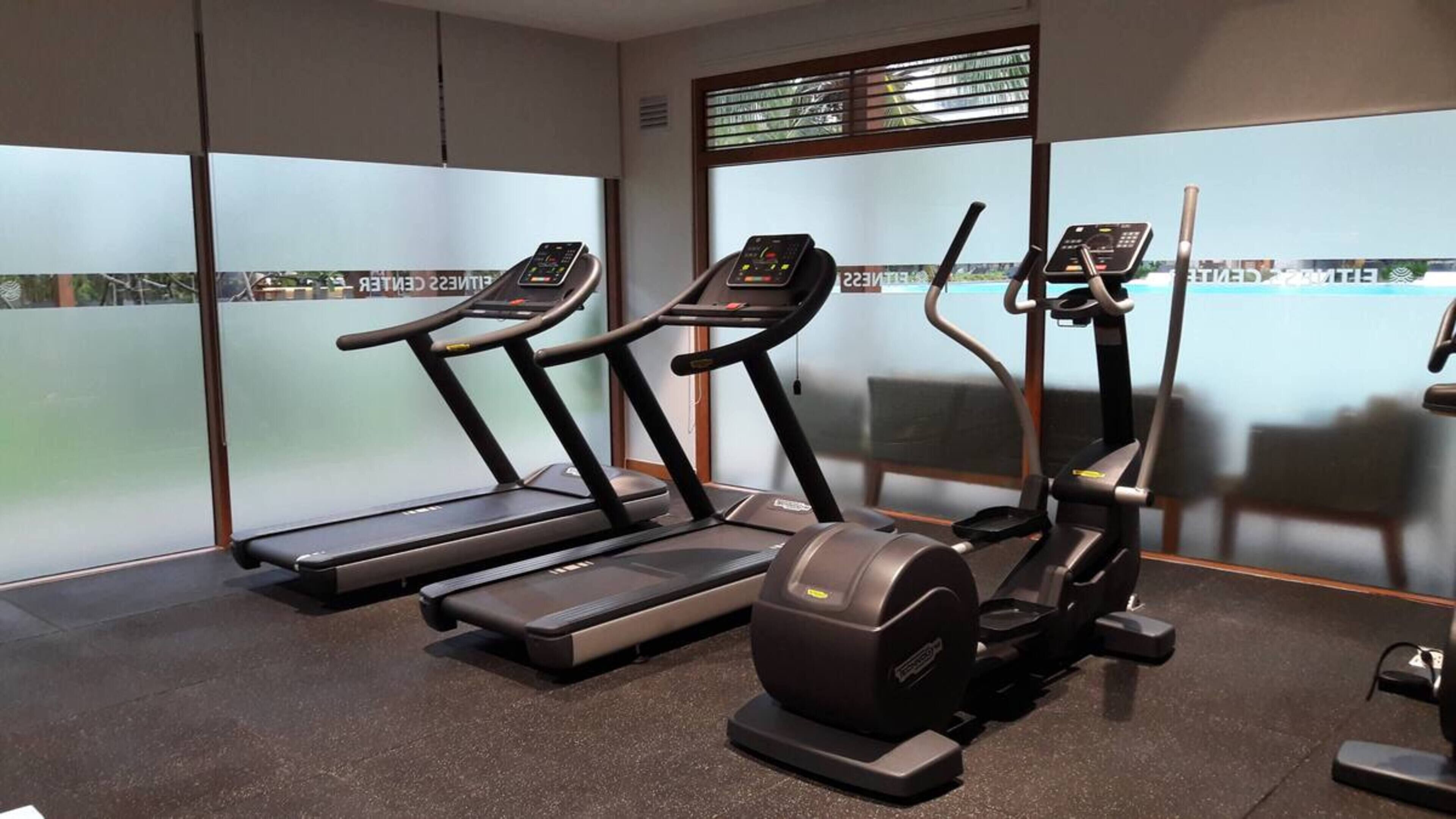 Un gimnasio con cintas de correr, una bicicleta estática y una máquina de remo.