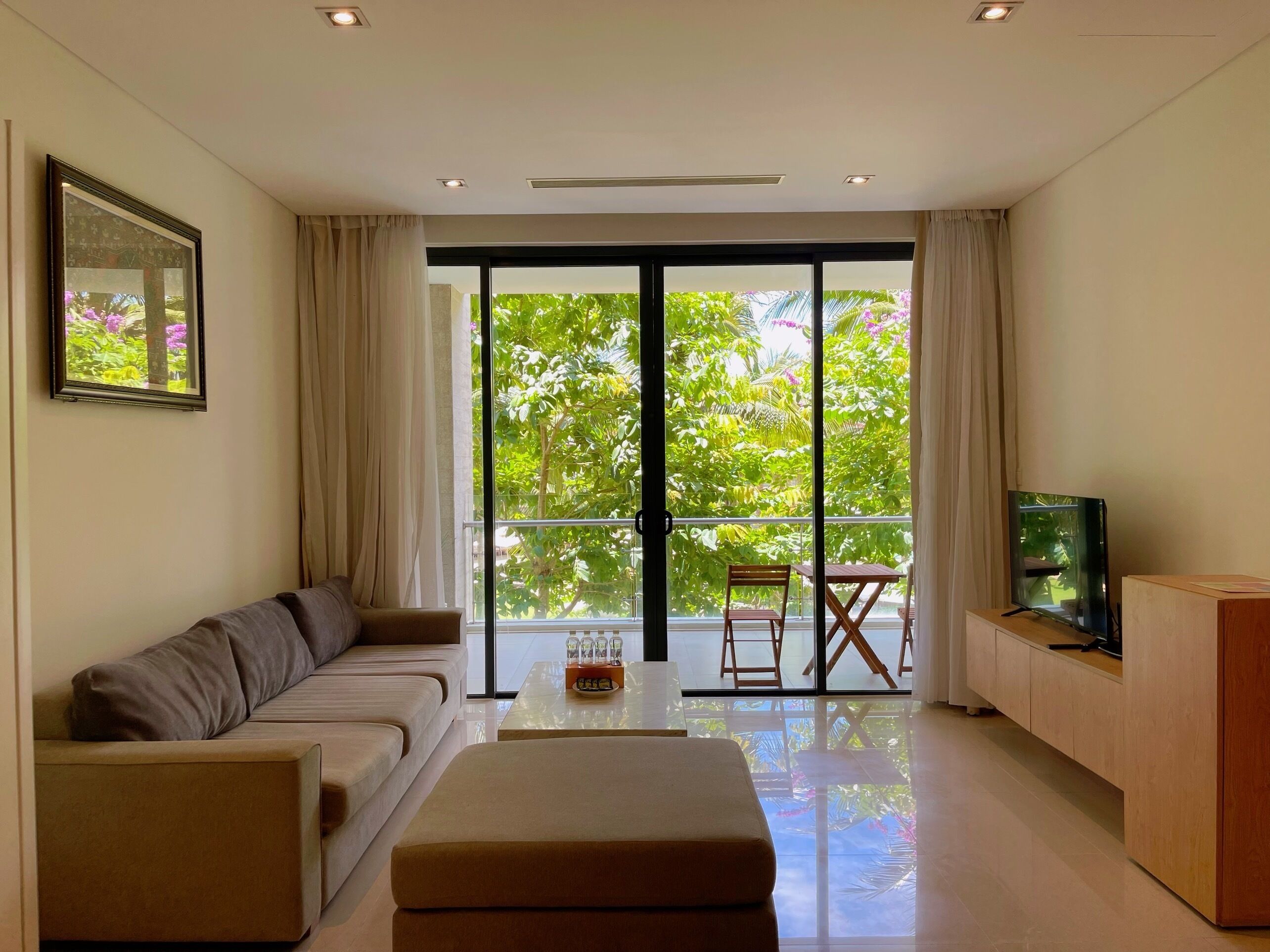 Una sala de estar moderna con sofá, una mesa de centro, televisor y un balcón con puertas de vidrio.