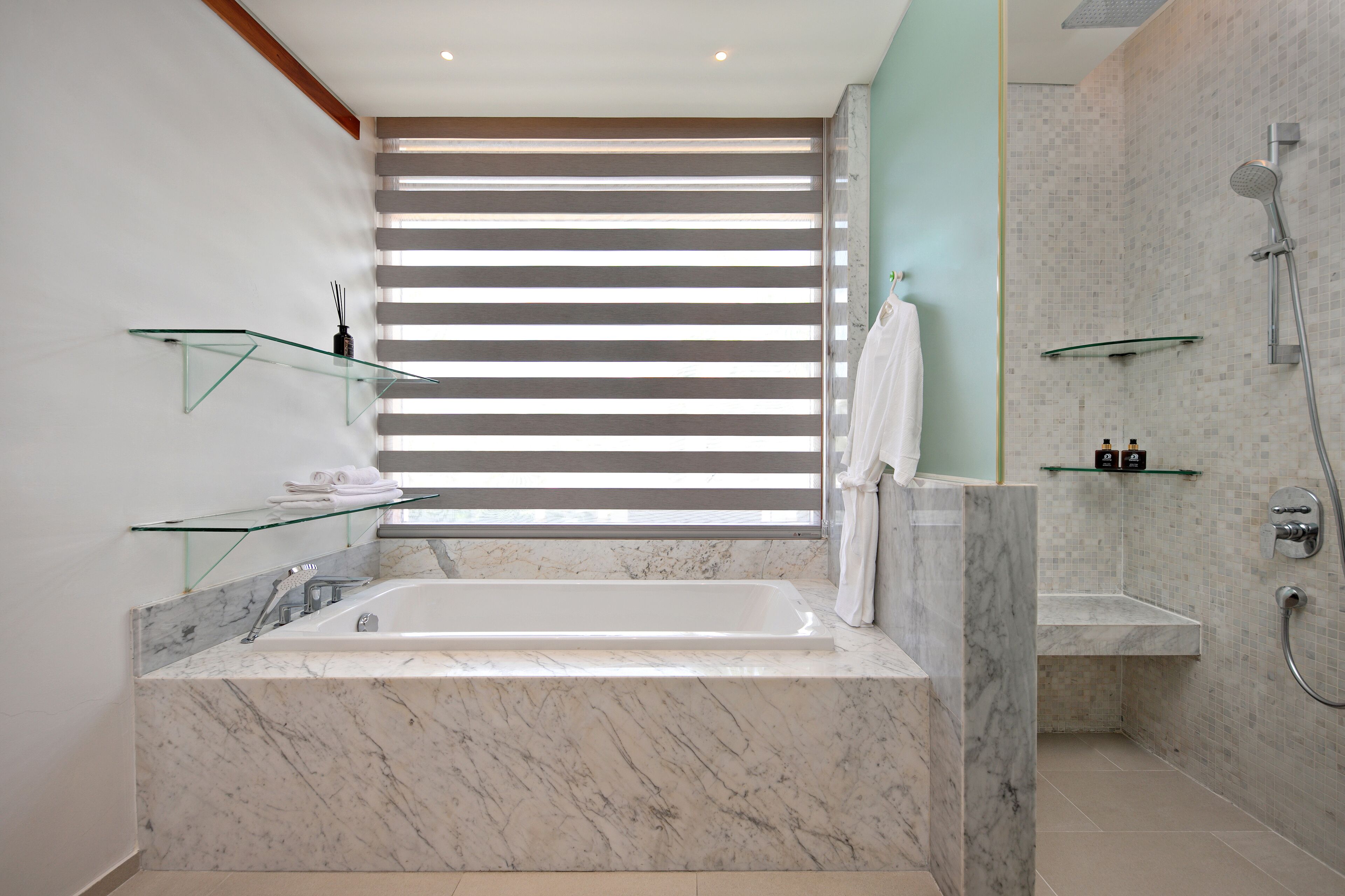 Un baño moderno con una bañera de mármol, repisas de vidrio y zona de ducha.