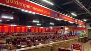 A spacious dining area with multiple tables and chairs, a prominent red and yellow color scheme, and a sign for goldenpalmerresort.co.uk. - Captivating Three Bedroom Caravan tv in Each Room (Skegness)