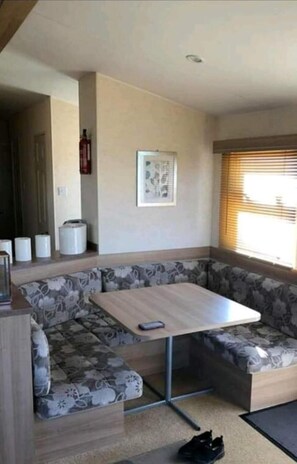 A compact living space with a sofa and a small table, a fire extinguisher, and a window with blinds.