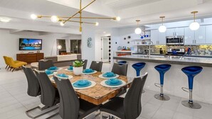 Una cocina moderna con una isla central, taburetes de bar y un comedor con mesa y sillas de madera.