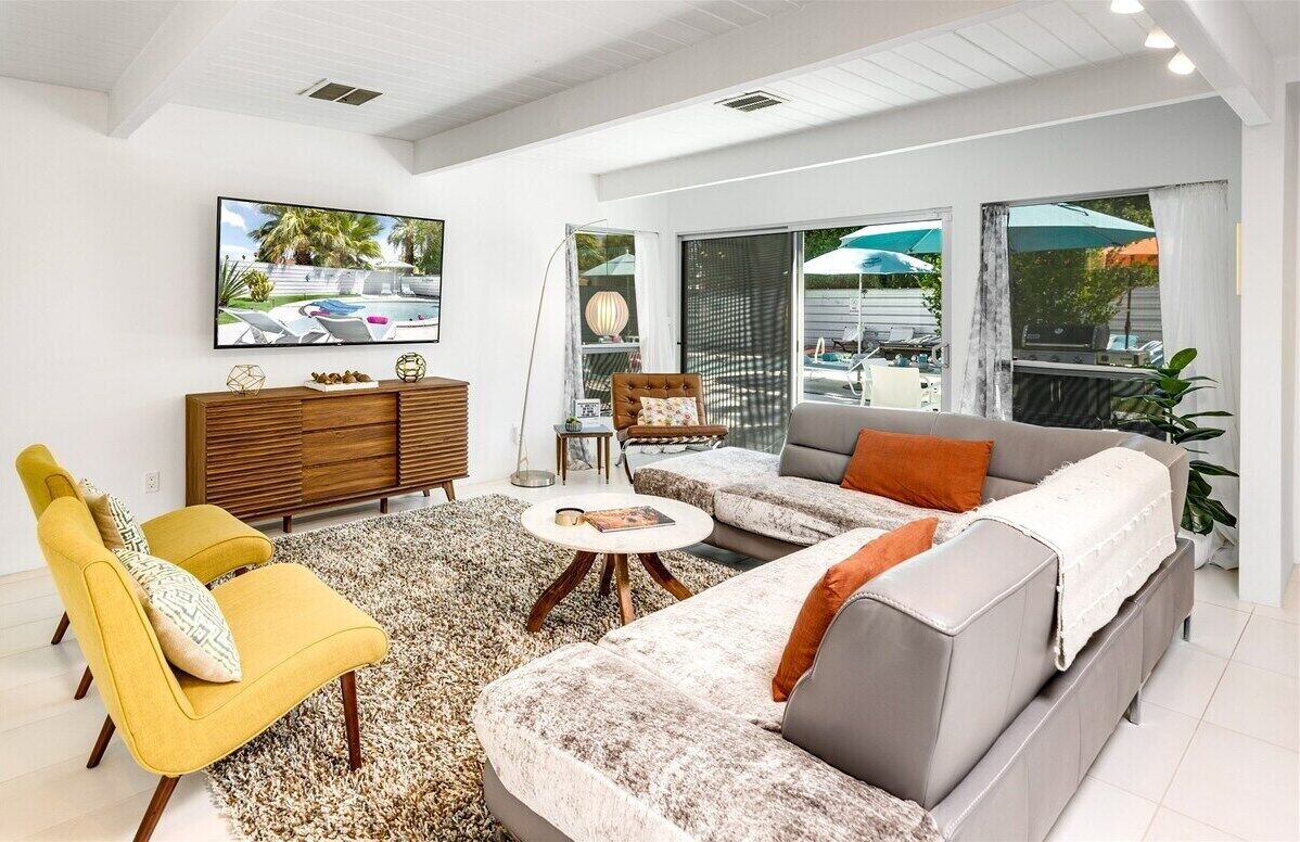 A modern living room with a sofa, armchairs, a coffee table, and a TV on the wall.