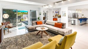 Una sala de estar moderna con un sofá modular, una mesa de centro y un sillón amarillo. Hay una puerta de vidrio que da a un balcón.
