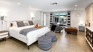 Una habitación de hotel moderna con una cama grande, una zona de estar con una silla y reposapiés, una mesita y vistas al exterior.