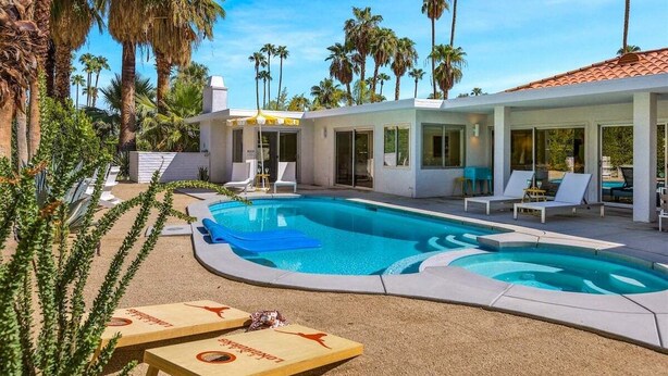 A pool area with lounge chairs and a modern building with large windows. - Blue Door at Indian Canyons – Mid-Century Retreat with Pool, Spa, Golf Course and Mountain Views (Palm Springs)